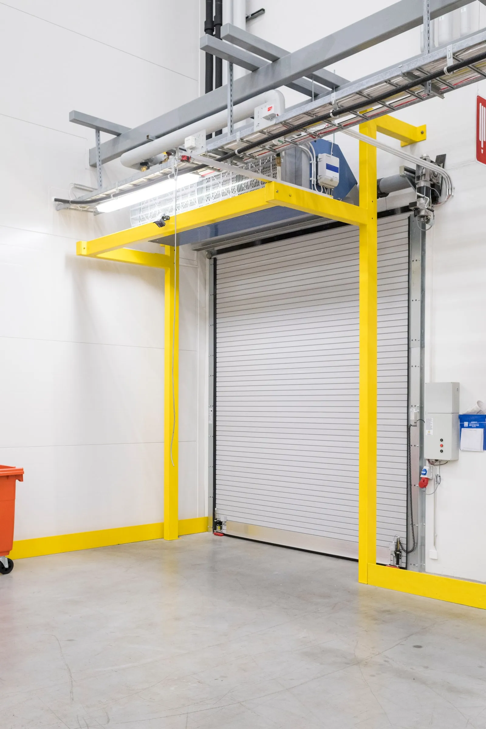 A high-speed industrial door in a yellow protective frame in the corner of a white space